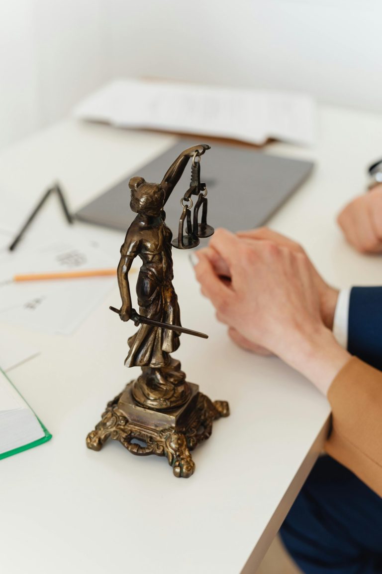 FAQ Bronze Lady Justice statue on a white office desk with hands in the background. Symbol of law and fairness.